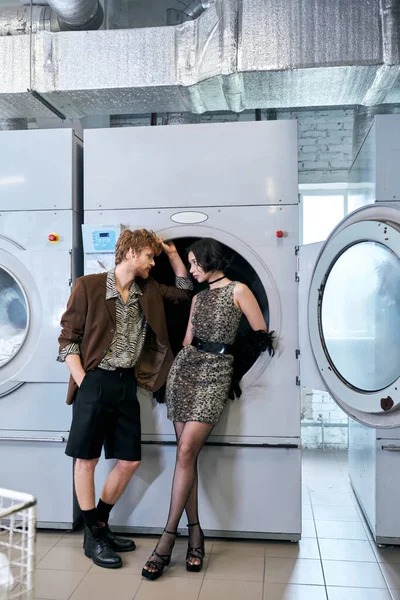 Vista laterale della giovane coppia multietnica alla moda che si guarda in lavanderia pubblica — Foto stock