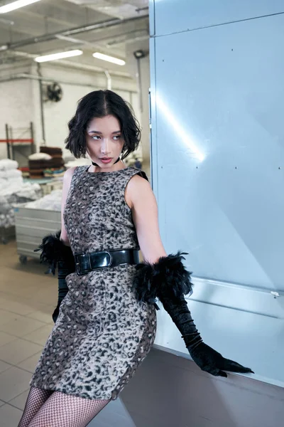 Trendy young asian woman in dress with animal print and gloves standing in public laundry — Stock Photo