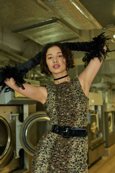 Confident young asian woman in gloves and dress posing and looking at camera in public laundry — Stock Photo