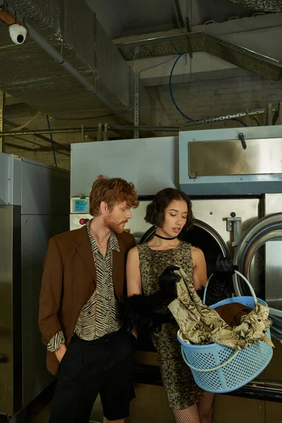 Stylish young asian woman holding basket with clothes near boyfriend in public laundry — Stock Photo