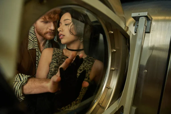 Jovem elegante posando com sexy asiático namorada atrás máquina de lavar roupa na lavanderia moeda — Fotografia de Stock