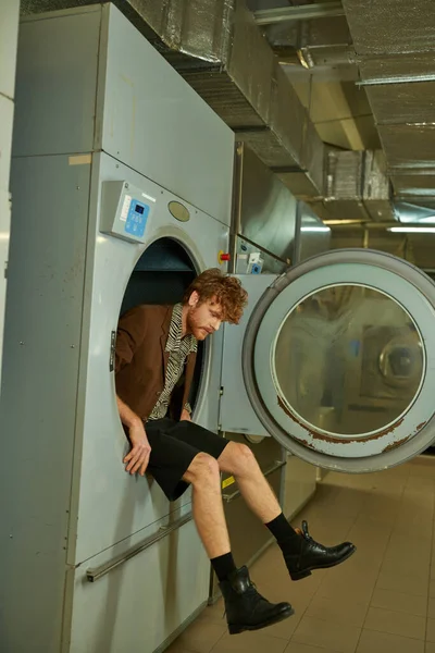 Homme à la mode et moderne dans la veste assis dans la machine à laver dans la blanchisserie à pièces — Photo de stock