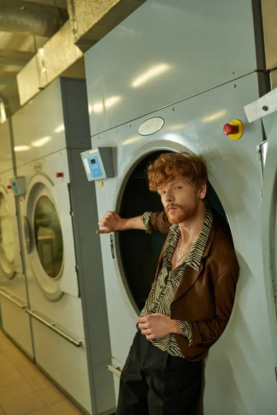 Confiant et élégant jeune homme en veste posant dans la machine à laver dans la buanderie publique — Photo de stock