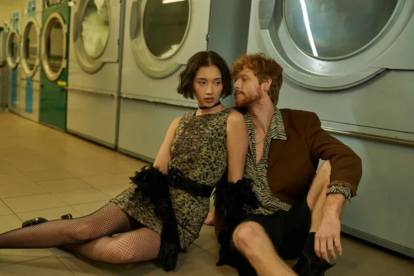 Young and modern interracial couple posing together on floor in public laundry in evening — Stock Photo