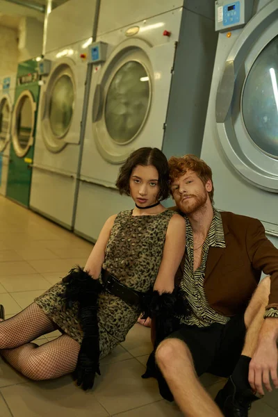 Moda jovem casal interracial olhando para a câmera enquanto posando na lavanderia pública à noite — Fotografia de Stock