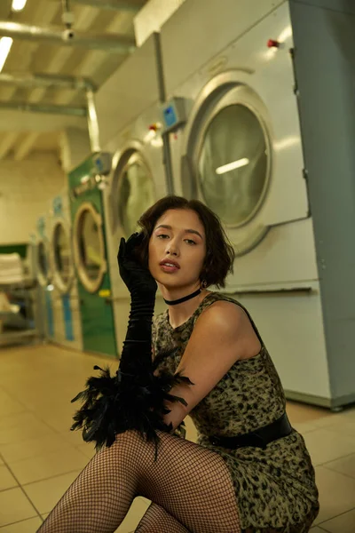 Mode jeune asiatique femme en robe regardant caméra tout en posant en self service blanchisserie — Photo de stock