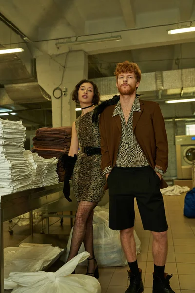 Fashionable young asian woman in dress posing near redhead boyfriend in public laundry — Stock Photo