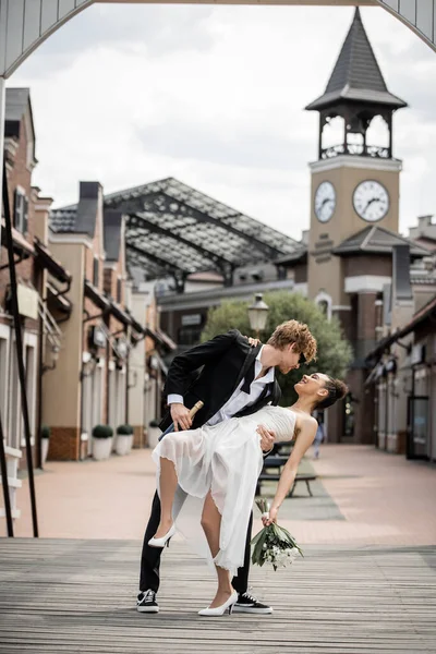 Cerimonia nuziale nella moderna città europea, giovane uomo che abbraccia felice sposa afro-americana in strada — Foto stock