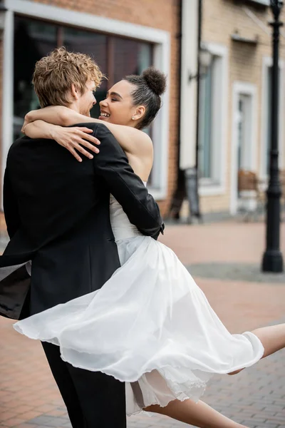 Outdoor wedding ceremony, delighted and stylish interracial couple embracing on city street — Stock Photo