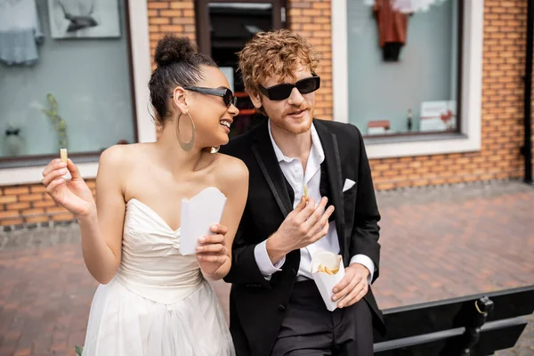 Outdoor wedding, snacking, stylish interracial couple, elegant attire, sunglasses, french fries — Stock Photo