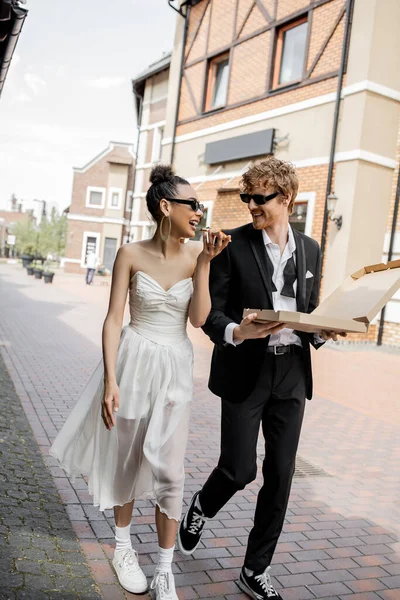 Urban romance, wedding in city, romantic interracial couple walking with pizza on street — Stock Photo