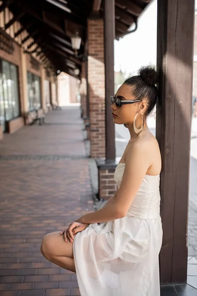 Side view of charming african american woman in wedding dress and sunglasses on urban street — Stock Photo