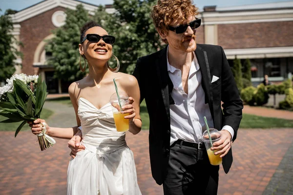 Casal interracial, óculos de sol, traje de casamento, suco de laranja, flores, felicidade, casamento ao ar livre — Fotografia de Stock