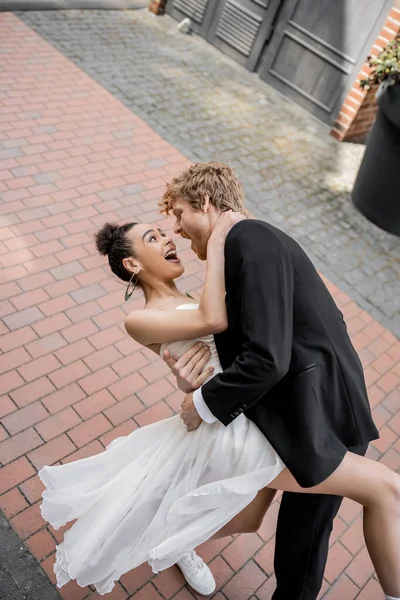 Молодий елегантний наречений обіймає схвильовану афроамериканську наречену, весілля в європейському місті — стокове фото