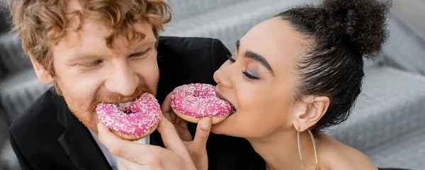 Elegant interracial couple feeding each other with sweet donuts, wedding on street, fun, banner — Stock Photo