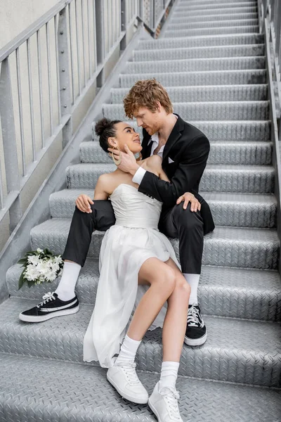 Urban romance, love, outdoor wedding, young interracial couple embracing near flowers on stairs — Stock Photo