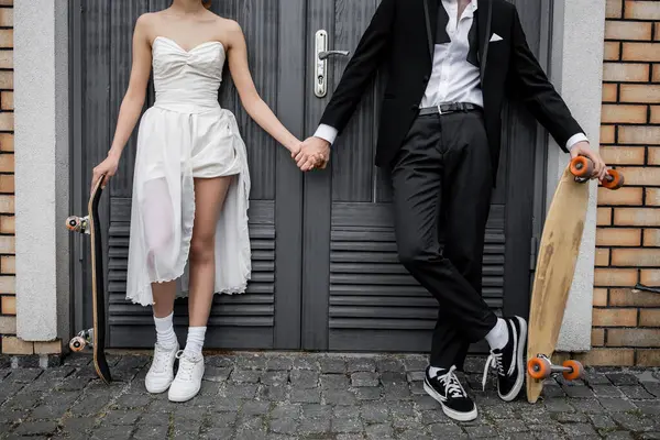 Interracial couple in wedding attire, with longboard and skateboard near city building, cropped view — Stock Photo