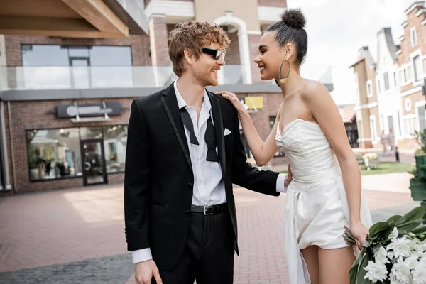 Outdoor wedding, modern and stylish interracial newlyweds looking at each other on street — Stock Photo