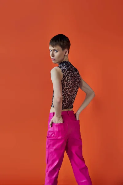 Moda queer, persona no binaria posando con las manos en bolsillos de pantalones de color rosa, animal print, patrón - foto de stock