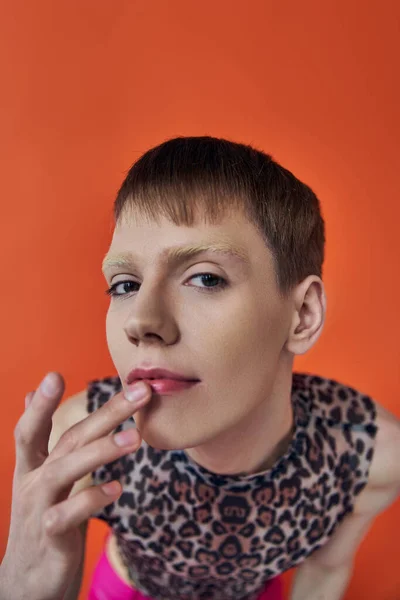 Nonbinary person smiling and touching lips on orange backdrop, looking at camera, queer fashion — Stock Photo