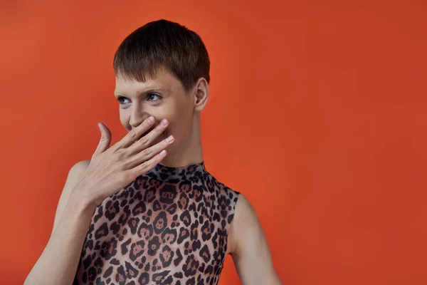 Shy nonbinary person smiling and covering mouth on orange backdrop, looking away, queer fashion — Stock Photo