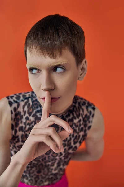 Nonbinary person in leopard print outfit showing hush sign on orange backdrop, queer fashion — Stock Photo