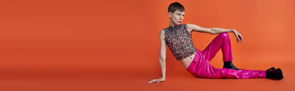 Personne non binaire en léopard imprimé haut et pantalon rose sur fond orange, mode queer, bannière — Photo de stock