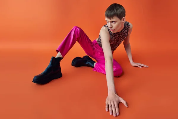 Queer Person in Leopardenmuster Top und rosa Hose sitzt auf orangefarbenem Hintergrund, Stil und Mode — Stockfoto