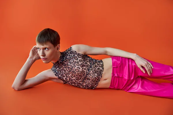 Persona queer in top stampa leopardo e pantaloni rosa sdraiati su sfondo arancione, stile e moda — Foto stock
