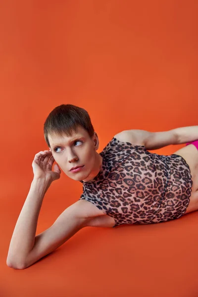 Queer persona en leopardo imprimir sin mangas superior acostado sobre fondo naranja, mirar hacia otro lado, estilo y moda - foto de stock