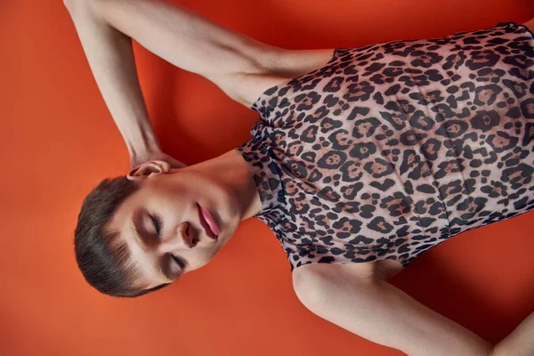 Queer persona en leopardo imprimir sin mangas superior acostado sobre fondo naranja, vista superior, estilo y moda - foto de stock