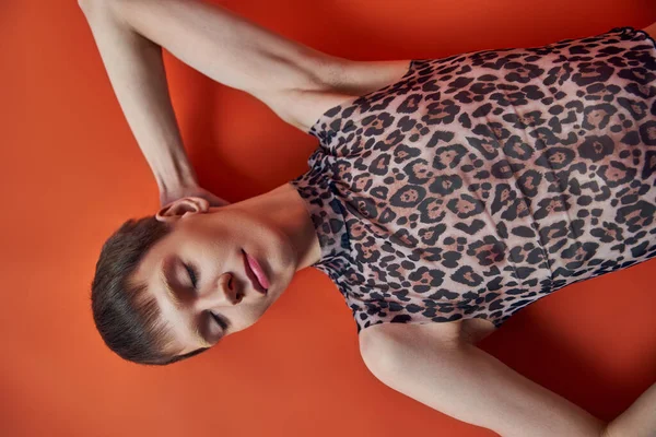 Queer persona en leopardo imprimir sin mangas superior acostado sobre fondo naranja, vista superior, estilo y moda — Stock Photo