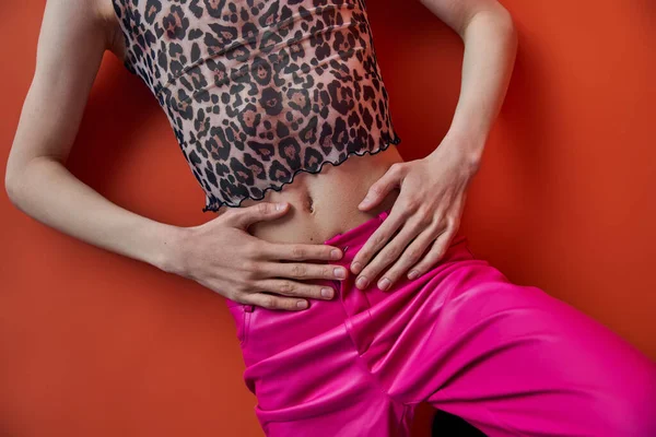 Queer Person in Leopardenmuster-Oberteil und rosa Hose auf orangefarbenem Hintergrund liegend, Draufsicht, Schnitt, Mode — Stockfoto