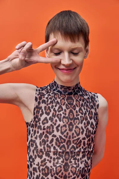 Fröhliche queere Person in Leopardenmuster ärmelloses Oberteil mit V-Zeichen auf orangefarbenem Hintergrund, lächeln — Stockfoto