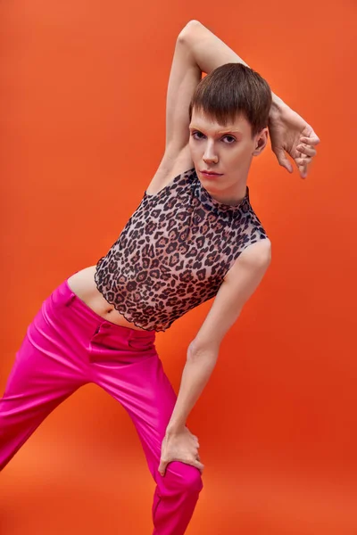 Modelo queer en estampado de leopardo sin mangas top y pantalones rosas posando, fondo naranja, tendencia de la moda - foto de stock