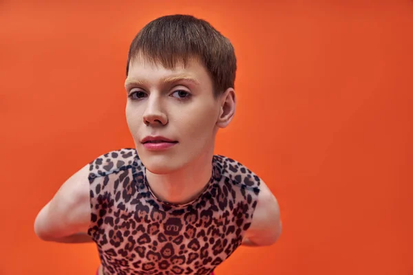 Modèle queer en léopard imprimé haut sans manches regardant la caméra, fond orange, tendance de la mode — Photo de stock