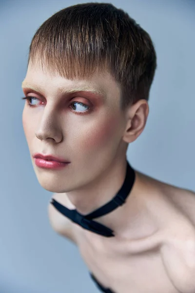 Modelo queer con maquillaje mirando hacia otro lado, fondo gris, moda, pajarita, andrógino, retrato - foto de stock