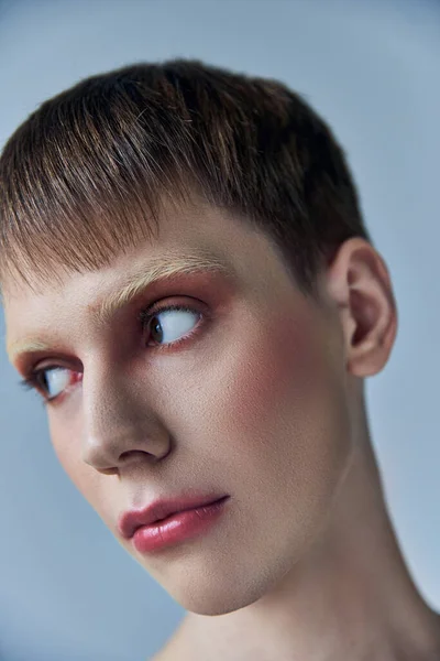 Queer pessoa com maquiagem olhando para longe, fundo cinza, beleza e visagem, andrógino, retrato — Fotografia de Stock