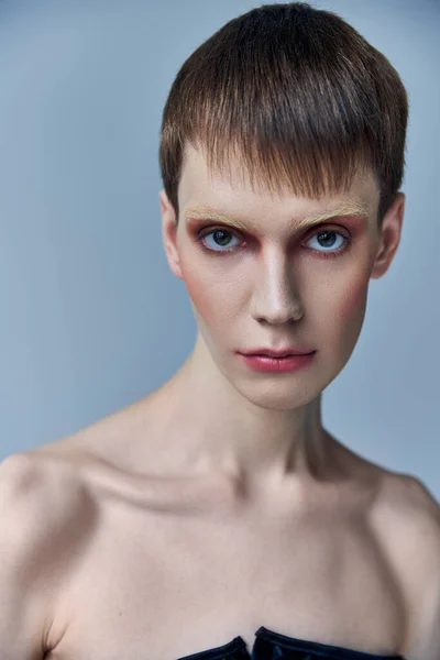 Androgynous person with makeup looking at camera, grey backdrop, beauty and visage, queer, portrait — Stock Photo