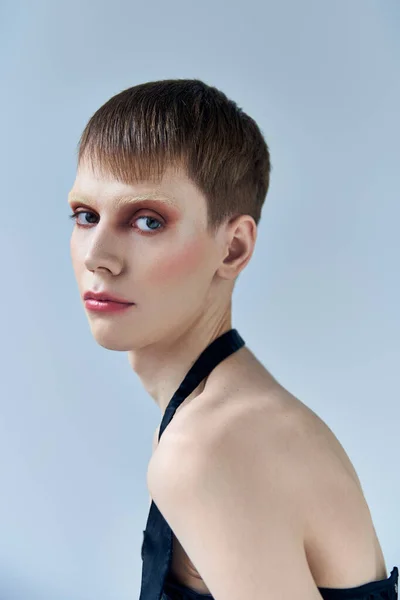 Androgynous model with makeup looking at camera, grey backdrop, beauty and visage, queer, portrait — Stock Photo