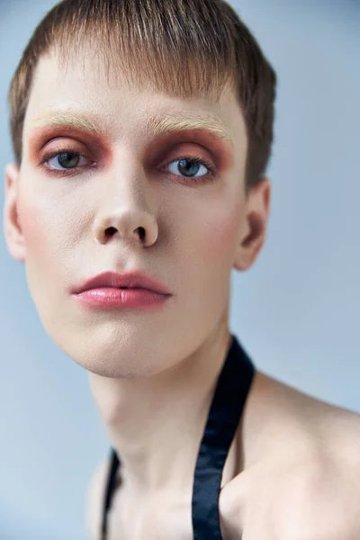 Nahaufnahme, androgyne Person mit Make-up, grauem Hintergrund, Schönheit und Visage, queer, Blick in die Kamera — Stockfoto