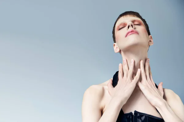 Porträt, queeres Model mit Make-up, das den Hals berührt und auf grauen, androgynen, geschlossenen Augen posiert — Stockfoto