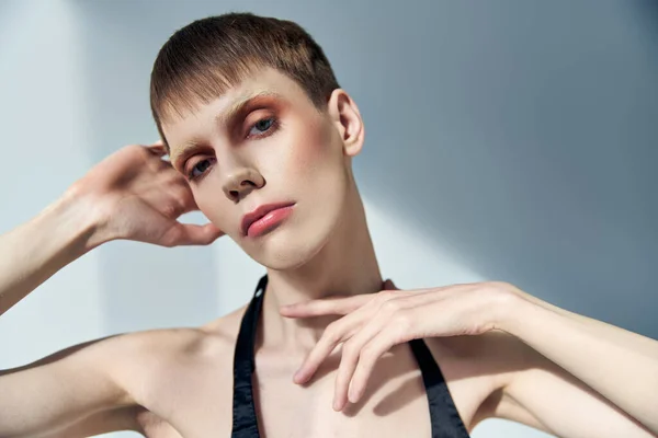Queer Person mit Make-up posiert auf grauem Hintergrund, Schönheit, Visage, androgynes Modell, Blick in die Kamera — Stockfoto