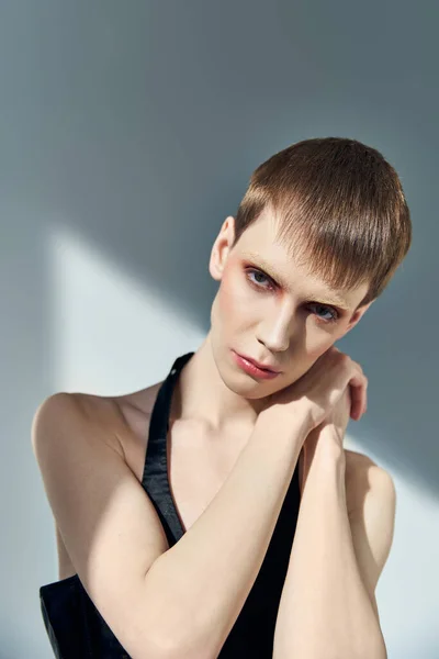 Queer Person mit Make-up posiert auf grauem Hintergrund, Schönheit, einzigartiges, androgynes Modell, Blick in die Kamera — Stockfoto