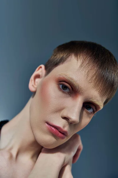 Queer model with makeup posing on grey backdrop, beauty, androgynous, look at camera, close up — Stock Photo
