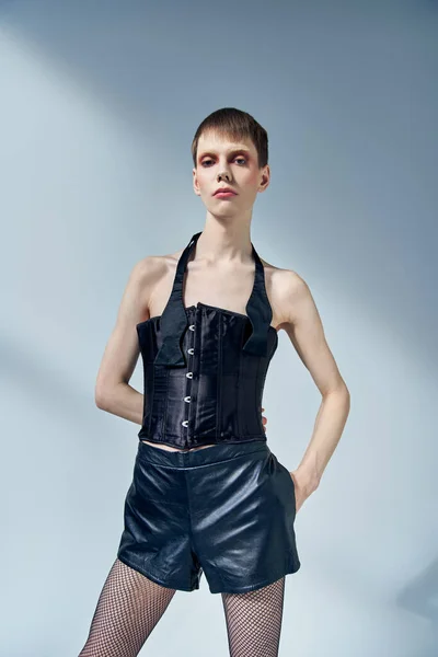 Queer model in black corset and shorts posing on grey backdrop, androgynous, hand in pocket — Stock Photo