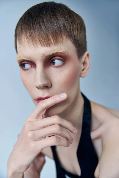 Modèle queer avec maquillage regardant loin sur fond gris, personne androgyne, portrait, identité — Photo de stock