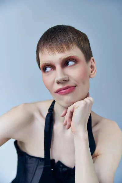 Queer person with makeup looking away on grey, androgynous model, self expression, skeptical — Stock Photo