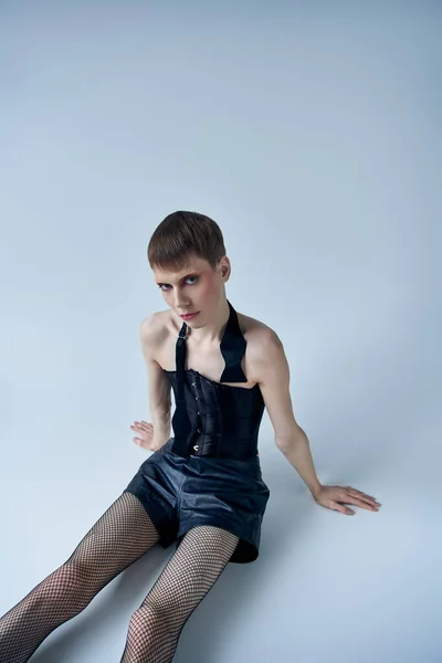 Queer model in black corset, boots, fishnet tights sitting on grey, androgynous person, lgbt, banner — Stock Photo