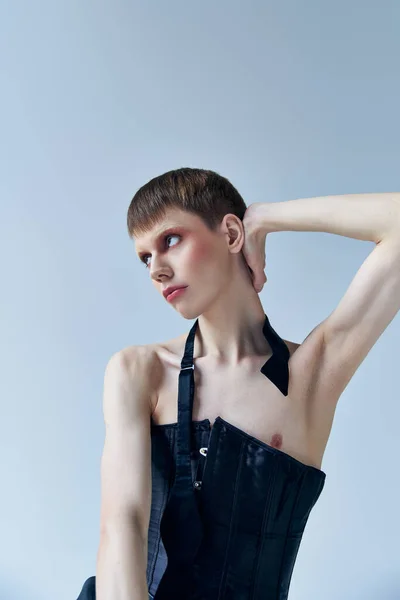 Androgynous model in black corset posing on grey, lgbt, queer fashion, looking away, self expression — Stock Photo